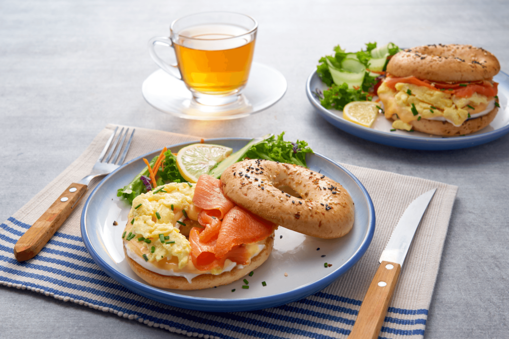 Smoked Salmon and Scrambled Eggs Breakfast Bagel with Side Salad and Tea on a Cement Table