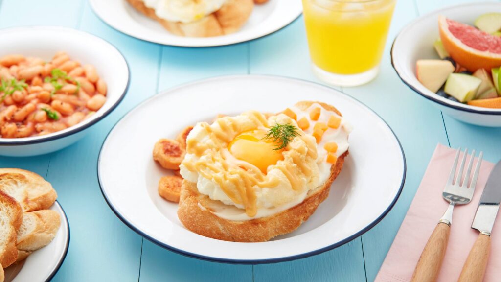 Cloudy Eggs with Sausages and Carrots, Baked Beans, Fruit Salad and Juice on a Blue Table