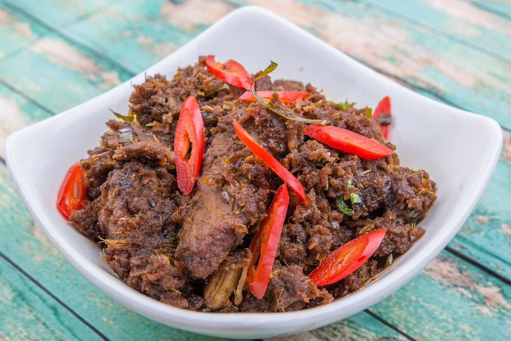 Rendang tok yang dihidangkan di dalam pinggan putih di atas meja makan berwarna rona biru.